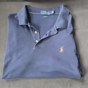 Blå pikétröja från Ralph Lauren - Säljer nu denna blåa piké från Ralph Lauren i storlek S, slim fit på denna mörkblåa pikén, inga defekter, alldeles perfekt för dig som köper kläder inför sommaren!