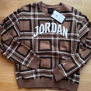 Brun rutig tröja från Jordan - Säljer en snygg brun rutig tröja från Jordan med vit text på bröstet. Tröjan har långa ärmar och en klassisk rund halsringning. Perfekt för en avslappnad stil. 🏀