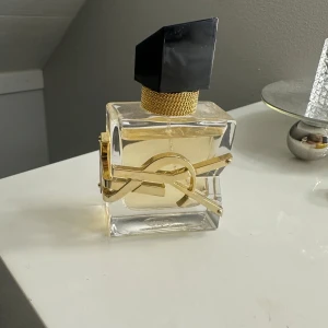 Yves Saint Laurent Libre Eau de Parfum - Säljer en elegant flaska av Yves Saint Laurent Libre Eau de Parfum. Flaskan har en unik design med en svart asymmetrisk kork och en gyllene YSL-logga runt den genomskinliga glasflaskan. Doften är känd för sin fräscha och blommiga karaktär. nypris 1400 säljer för 650💗