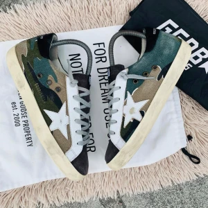 Camouflage sneakers från Golden Goose - Snygga sneakers från Golden Goose med ett coolt camouflage-mönster i grönt, beige och blått. Skorna har en vit stjärna på sidan och grå snörning. Perfekta för en avslappnad stil med en touch av unik design. Storlek 39 passar 40-41.