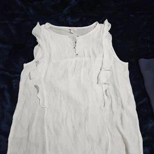 Vit blus från Esprit - Säljer en elegant vit blus från Esprit med volangdetaljer vid ärmarna. Blusen har en rund halsringning och en liten knapp framtill. Perfekt för en stilren look.