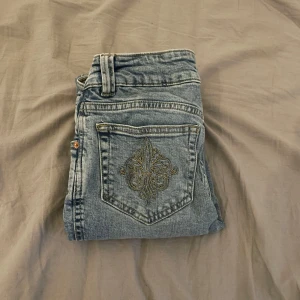 Blå jeans med broderad detalj - Snygga blå jeans med hög midja och broderade detaljer på bakfickorna,flare och low waist. Använt en gång. Pris kan diskuteras 