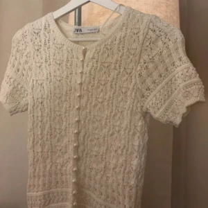 Vit stickad kofta från Zara - Charmig vit stickad kofta från Zara med korta ärmar och fina knappar framtill. Perfekt för en stilren och mysig look. Den har ett vackert mönster som ger en elegant touch.