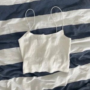 Vit ribbad linnetopp från H&M - Säljer en stilren vit ribbad linnetopp från H&M Divided. Toppen har tunna axelband och en croppad passform, perfekt för varma dagar. Enkel och lätt att matcha med olika outfits.
