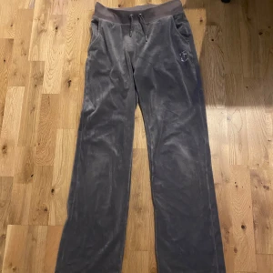 Gråa mjukisbyxor från Juicy Couture - Snygga gråa mjukisbyxor från Juicy Couture med glittrande stenar som bildar texten 'Juicy' på baksidan. Superfina men används inte längre. Der används en del, har tappat två stenar på baksidan som syns på bild 3-5🤍🤍