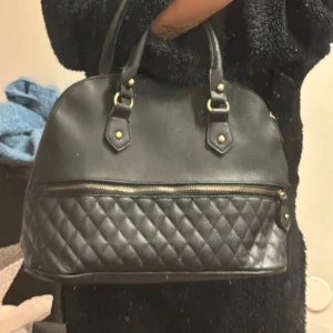 Svart quiltad handväska - Snygg svart handväska med quiltad design och dragkedja. Väskan har två handtag och guldfärgade detaljer. Pris kan diskuteras vid snabbt affär