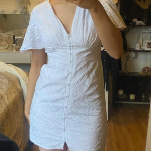 Studentklänning / Vit klänning med knapp detaljer - Säljer en söt vit klänning med v-ringning och knappar framtill. Klänningen har korta ärmar och ett fint broderat mönster. Perfekt för sommarens alla tillfällen! perfekt till studenten som studentklänning