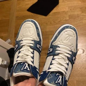 Blå och vita sneakers från Louis Vuitton - Snygga sneakers i blått och vitt från Louis Vuitton med märkets ikoniska monogrammönster. Skorna har snörning och en robust sula med tydlig logotyp. Perfekta för den som vill ha en stilren och lyxig look.