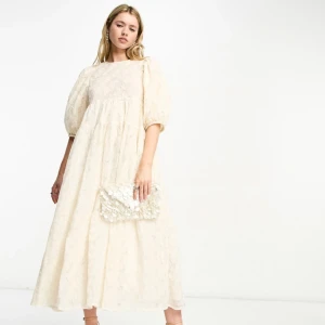 Champagnefärgad klänning med blommigt mönster - Säljer en elegant champagnefärgad långklänning med ett vackert blommigt mönster. Klänningen har puffiga trekvartsärmar och en luftig passform som ger en somrig, söt vibe. Perfekt för speciella tillfällen såsom studenten/midsommar. Den är helt ny med prislapp. Dream Sister Jane. Ärmarna har insydda pärlor. 