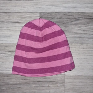 Rosa och lila randig mössa - Snygg och färgglad mössa i rosa och lila med breda ränder. Perfekt för att hålla värmen under kyliga dagar. Den är mjuk och bekväm att bära.