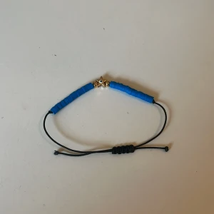 Blått armband med stjärndetalj - Snyggt armband med blå pärlor och en guldfärgad stjärna i mitten. Armbandet har en justerbar svart snörning för perfekt passform. Köpt i Grekland 🇬🇷 