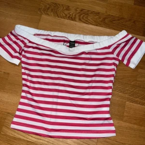 Randig offshoulder topp från Shein - Säljer en snygg randig offshoulder topp från Shein i rosa och vitt. Toppen har korta ärmar och en bekväm passform som passar perfekt för sommardagar. Perfekt för en avslappnad och stilren look.
