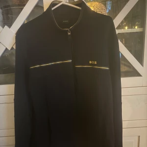 Svart jacka från Boss - Snygg svart jacka från Boss med dragkedja och subtila detaljer i guld. Perfekt för en stilren look. Jackan har långa ärmar och en enkel design som passar till många tillfällen. Storlek Xl bra i storlek. Kontakta mig för frågor😃