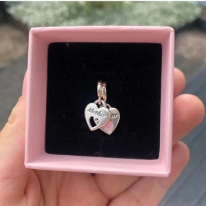 Silverfärgat hjärthalsband - Charmigt silverfärgat halsband med två hjärtformade hängen. Ena hjärtat har texten 'Mom' och ett utskuret hjärta. Perfekt som en kärleksfull present.