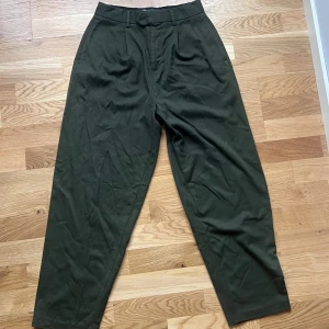 Mörkgröna byxor från ASOS DESIGN - Snygga mörkgröna byxor från ASOS DESIGN med hög midja och en klassisk passform. Byxorna har en stilren design med knäppning fram och två bakfickor med knappar. Aldrig använda!