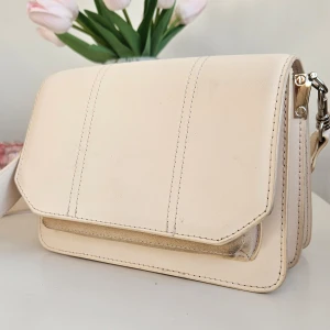 Ljusrosa axelväska från NA-KD  - Lite missfärgad på framsidan, under flärpen samt Lite märken inuti väskan. Annars är den  i väldigt fint skick. Färgen är väldigt ljusrosa nästan lite beige.