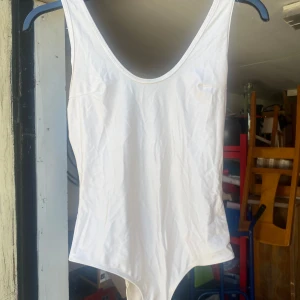 Vit baddräkt från BikBok - Säljer en stilren vit body från BikBok i storlek S. Den har en enkel och klassisk design med djup rygg. Materialet känns mjukt och bekvämt mot huden.