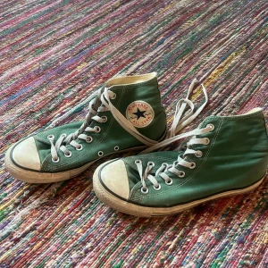 Gröna Converse All Star sneakers - Säljer ett par gröna Converse All Star sneakers i klassisk modell. De har en hög snörning och den ikoniska loggan på sidan. Skorna är i välanvänt skick med lite slitage på sulan och tån, men de är fortfarande supercoola och perfekta för en avslappnad stil.