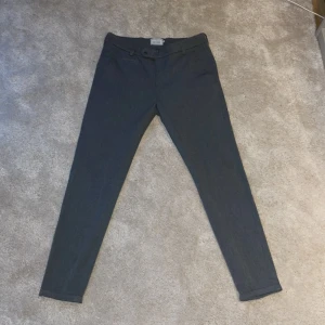 Grå byxor från Les Deux - Säljer ett par stilrena grå byxor från Les Deux. De har en midwaist passform och är gjorda i ett bekvämt material som känns skönt mot huden. Byxorna har en knapp och dragkedja framtill, vilket ger en klassisk look. Perfekta för både vardag och fest!