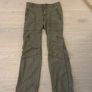 Lågmidjade cargopants - Säljer dessa jättesnygga cargopantsen då de inte kommer till användning. De hade ett hål på baksidan som har blivit ihopsytt av en skräddare (se 5,te bild) De är militärgröna/lite gråaktiga. Midjemått-38cm innerbenslängden-82cm. Sitter bootcut!❤️💕