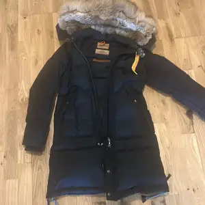 Säljer en svart dunjacka från Parajumpers, perfekt för kalla vinterdagar. Jackan har en fluffig pälsfodrad huva och långa ärmar. Den är en del av Masterpiece Series och har en dragkedja framtill. Supervarm och stilren!