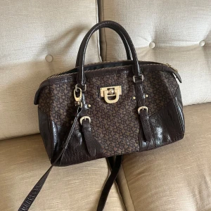 DKNY väska - Väska ifrån Dkny i bra skick🤎endast mindre slitningar vid kanterna. I brun färg med guld detaljer. 2 fickor för kort och 2 fickor med dragkedja på insidan av väskan. Går att bära både med kort och långt band!  Mått Bredd 41cm  Höjd 22cm  Djup 16cm  