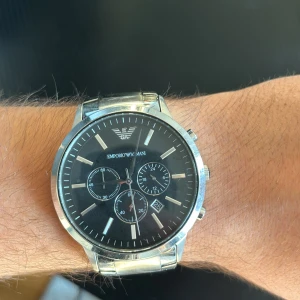 Emporio Armani klocka  - Emporio Armani klocka i stainless steel (rostfritt stål). Den har tidtagarur och datum som extra funktioner. Batteriet på klockan är slut. Bara att skriva vid funderingar.  