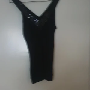 Svart klänning med paljetter - Snygg svart linne med glittriga paljetter längs v-ringningen. Perfekt för festliga tillfällen!