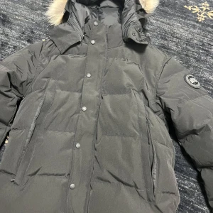 Canada goose  - Säljer en svart dunjacka från Canada Goose med pälsdetalj på huvan. Jackan har långa ärmar och stängs med både dragkedja och knappar. Perfekt för kalla vinterdagar. Storlek S blacklabel med bästa päls. Storlek s men kan också passa m
