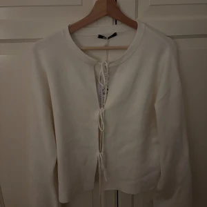 Vit stickad kofta från Gina Tricot - Säljer en stilren vit stickad kofta från Gina Tricot. Koftan har knytband framtill och långa ärmar, perfekt för lager-på-lager under kyligare dagar. Ett mångsidigt plagg som passar till många olika outfits. 