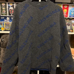 Grå tröja från Balenciaga - Säljer en snygg grå tröja från Balenciaga med blå logotypmönster över hela plagget. Tröjan har en klassisk rund hals och långa ärmar, perfekt för en stilren look.