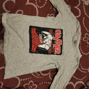 Grå långärmad tröja med gamer-tryck - Cool grå långärmad tröja från H&M med ett färgglatt gamer-tryck på framsidan. Perfekt för gaming-entusiaster som vill visa sin passion. Tröjan har en bekväm passform och är gjord i mjukt material.