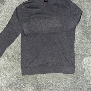 Grå tröja från Hugo Boss - Säljer en stilren grå tröja från Hugo Boss. Tröjan är långärmad och har en diskret logga på ryggen. Perfekt för en avslappnad men ändå elegant look.