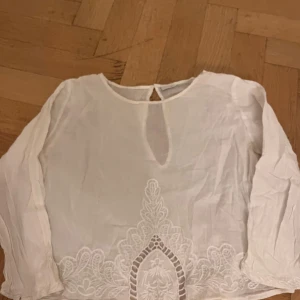 Vit blus från Gina Tricot - Passar mig som vanligtvis har XS Säljer en elegant vit blus från Gina Tricot med vackra spetsdetaljer längst ner. Blusen har långärmade och en liten öppning vid halsen. Perfekt för en stilren look.