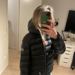 Svart dunjacka från Colmar - Säljer en svart pufferjacka från Colmar med huva i italiensk storlek 44 (motsvarande 36-38 el S-M).   Grå på insidan. Jättefint skick. 