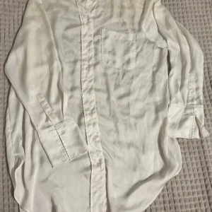 Vit långärmad skjorta - Säljer en klassisk vit långärmad skjorta med knappar och bröstficka. Perfekt för en stilren look. Om ni vill se den på, skriv gärna!