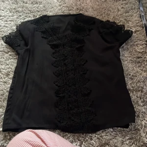 Svart blus med spetsdetaljer - Elegant svart blus med vackra spetsdetaljer längs framsidan och vid ärmarna. Perfekt för en fest eller finare middag. Storlek M men passar nog S också och Xs 