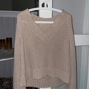Beige stickad tröja - Säljer en mysig beige stickad tröja med v-ringad design. Tröjan har långa stora ärmar och ribbade detaljer vid ärmslut och nederkant. Perfekt för kyliga dagar! 