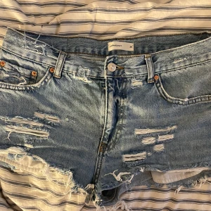 Blå jeansshorts - Snygga blå jeansshorts som jag gjort själv från ett par Gina Tricot jeans med slitna detaljer och fransiga kanter. Perfekta för en avslappnad sommarlook. De har en knapp och dragkedja framtill samt klassiska fem fickor.