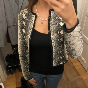 KOFTA MED ORMSKINNSMÖNSTER - Så snygg kofta med mönster. Har spännen så man kan knäppa koftan framtill också men som inte syns när man har den! Jag är 175 cm och koftan är i S. Hör av er vid frågor!! 