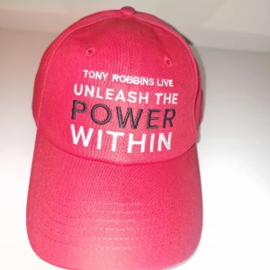 Tony Robbins röd keps - Tony Robbins keps med texten 'Unleash the Power Within' broderad framtill. Tillverkad i 100 % bomull och har justerbar passform. Garderobsrensning så kika gärna på övriga auktioner. 