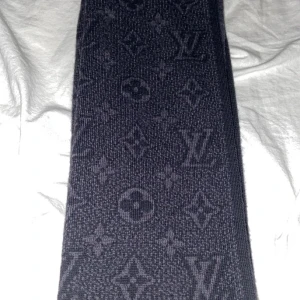 Svart halsduk från Louis Vuitton - Elegant svart halsduk från Louis Vuitton med det ikoniska monogrammönstret. Perfekt för att hålla stilen under kyliga dagar. Den har en lyxig känsla och är ett måste för modeälskare. Den är oanvänd och ny. Skick 10/10