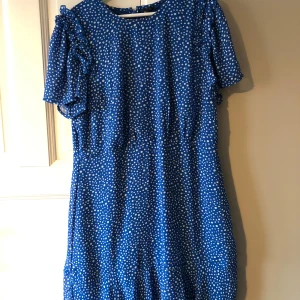 Blå prickig klänning från Vero Moda - Charmig blå klänning med vita prickar från Vero Moda. Klänningen har korta ärmar med volangdetaljer och en bekväm passform. Perfekt för en somrig look. Använd 2 gånger, fint med ett skärp till för att få en syndligare midja!