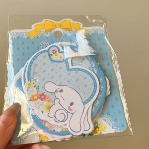 Cinnamoroll stickers från Sanrio - Sött anteckningsblock med Cinnamoroll-motiv från Sanrio. Blocket har en blå bakgrund med vita spetsdetaljer och en gul rosett. Perfekt för att skriva små meddelanden eller anteckningar. Kompakt och lätt att bära med sig.