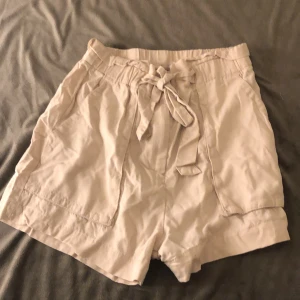 Beige shorts med knytband - Snygga beige shorts med knytband i midjan. Perfekta för en avslappnad sommarlook. De har en lös passform och är tillverkade i ett mjukt material för extra komfort.