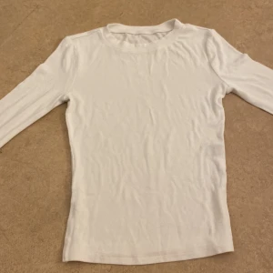 Vit ribbad långärmad tröja - Säljer en stilren vit ribbad tröja med långa ärmar. Perfekt för lager-på-lager eller som den är. Enkel och mångsidig design.