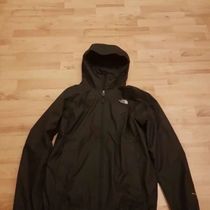 Svart vindjacka från The North Face - Säljer en svart vindjacka från The North Face i storlek m men är som s är liten i storleken . Jackan har en praktisk huva och dragkedja framtill. Perfekt för blåsiga dagar och utomhusaktiviteter.