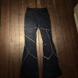 Svarta jeans med fransiga detaljer från Collusion - Snygga svarta jeans från Collusion med unika fransiga detaljer som ger en edgy look. Byxorna har en bootcut-stil och är väldigt unika och coola. De är High waist men man kan lätt sy om de till low waist om man föredrar det