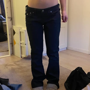Svarta jeans från True Religion - Snygga svarta jeans från True Religion med låg midja och bootcut-stil. Jeansen har dekorativa sömmar och knappar på bakfickorna. Perfekta för en trendig look.
