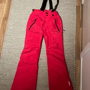 Rosa skidbyxor från Everest - Säljer ett par rosa skidbyxor från Everest med svarta detaljer och hängslen. Byxorna har dragkedjor vid fickorna och knäppning i midjan. Perfekta för vintersport och håller dig varm i backen. Hör av dig vid eventuella frågor💕